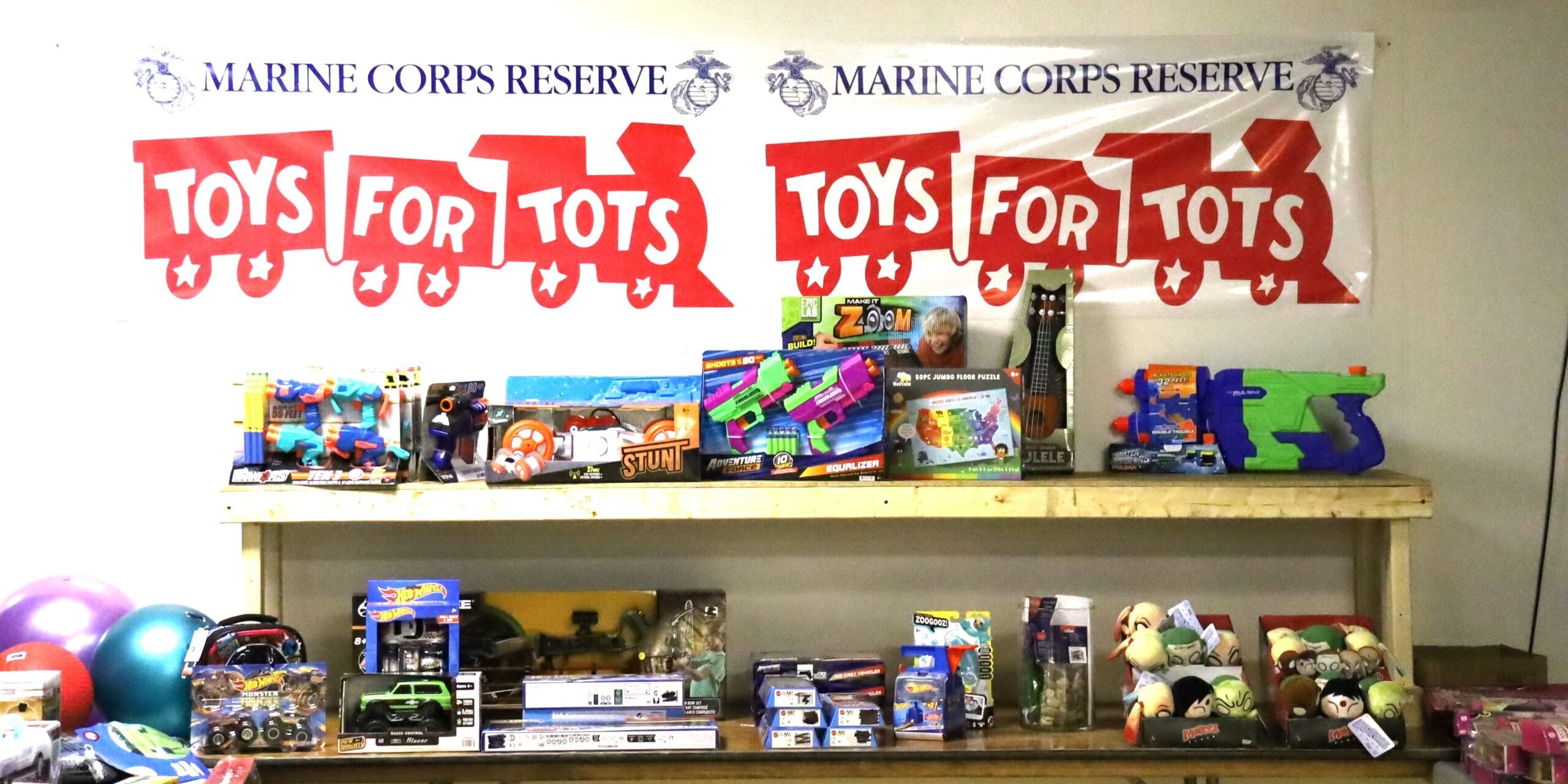 A "Toys for Tots" banner proudly displayed above a stack of donated toys for the 2023 Christmas season.