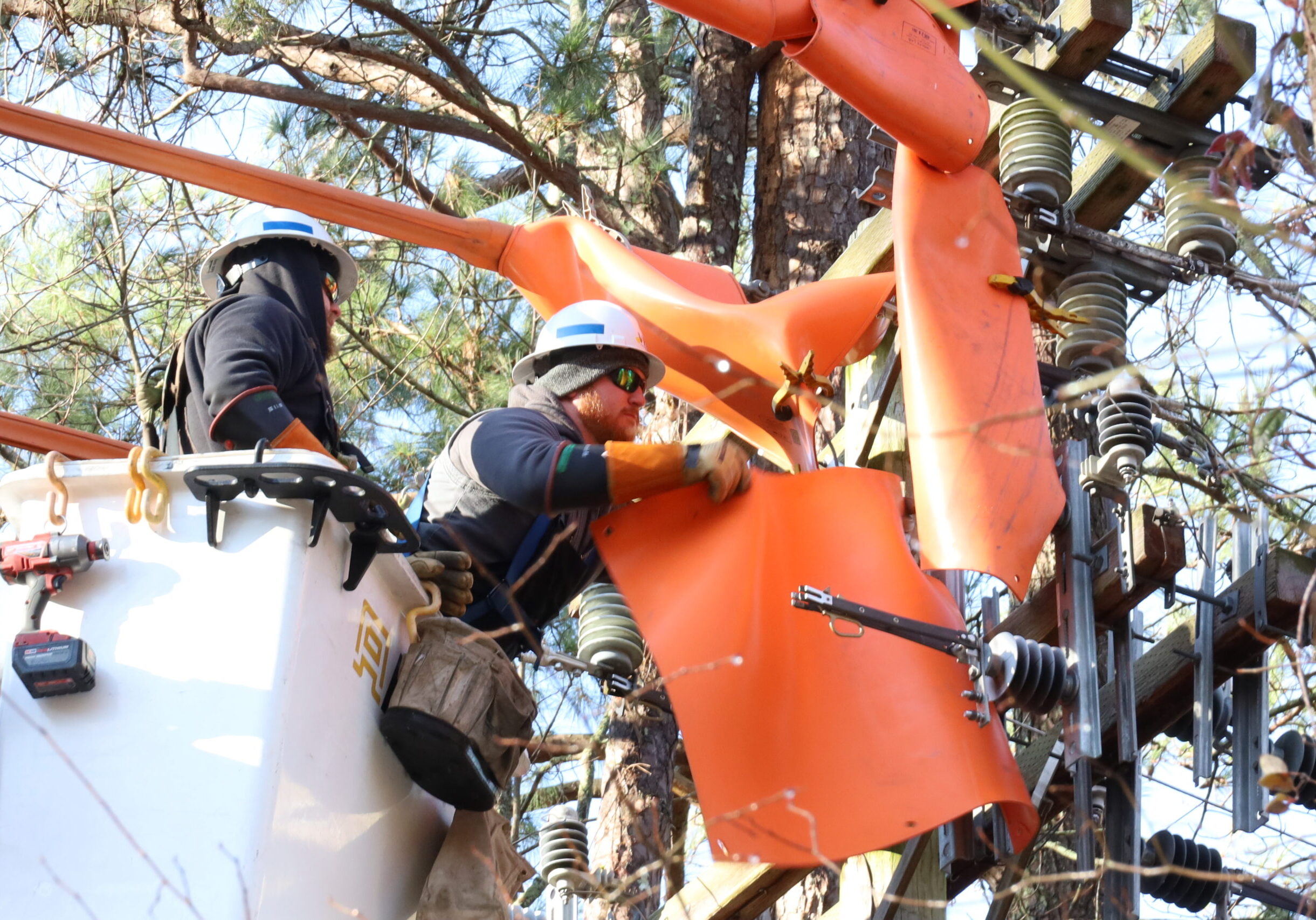 Tanner Swann (left) and Trevor Cartwright (right) secure orange rubber blankets to power lines.